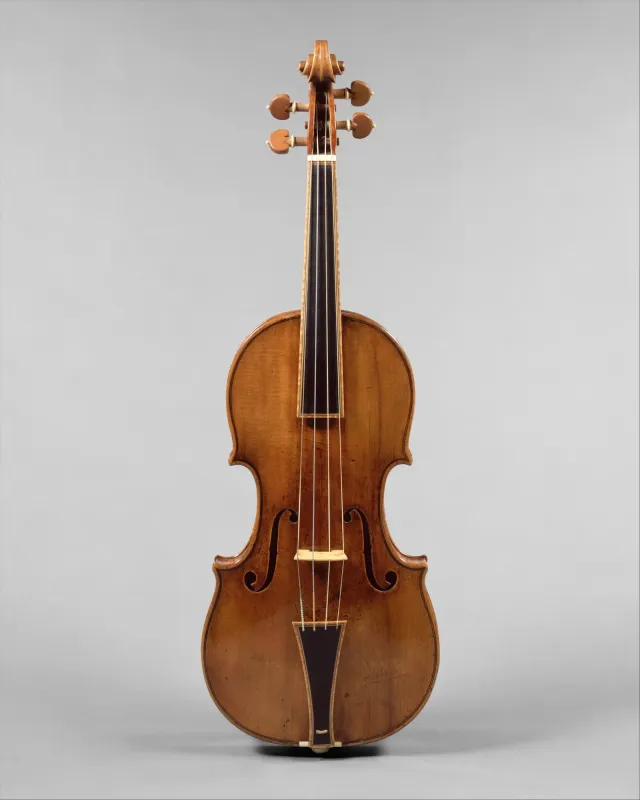 O violino Gould de Stradivari, de 1693, visto de frente sobre fundo cinza neutro: o tampo de abeto em verniz âmbar, os efes, o espelho e as quatro cravelhas da voluta.